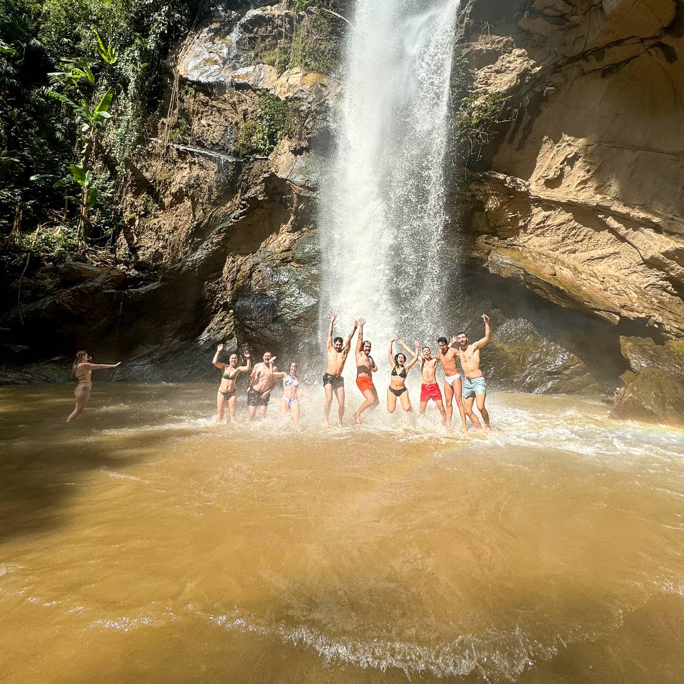 Group of hikers jumping under a jungle waterfall during a Chiang Mai trek.