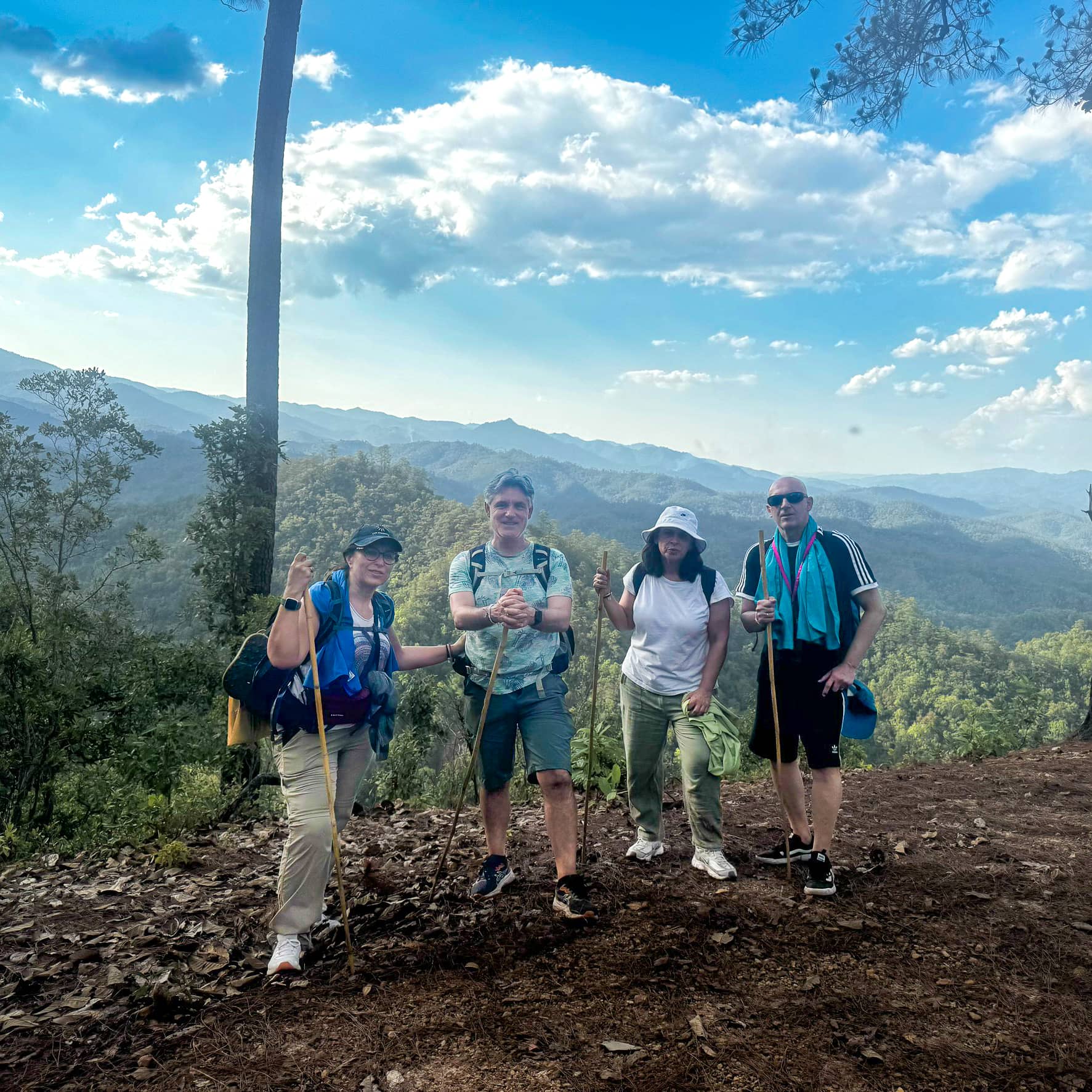 Trek group standing on a mountain ridge with scenic forested hills behind them.