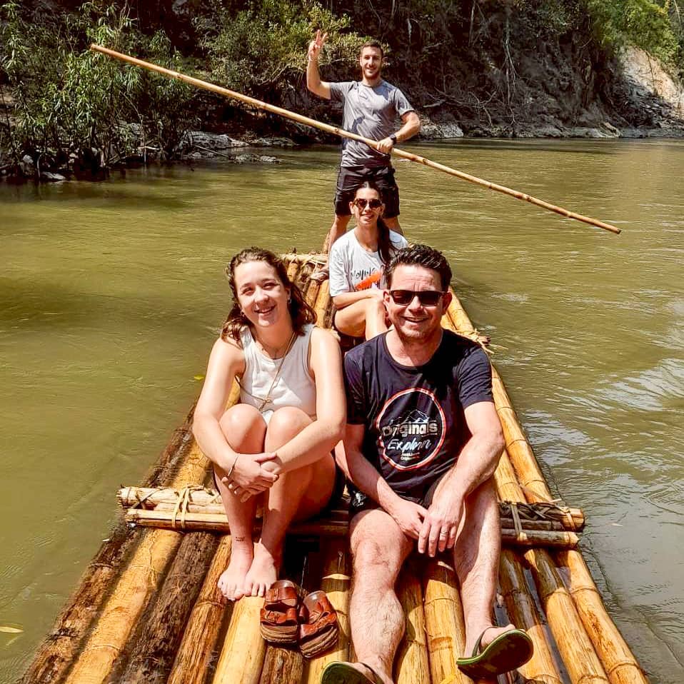 Travelers rafting down a calm jungle river on a bamboo raft.