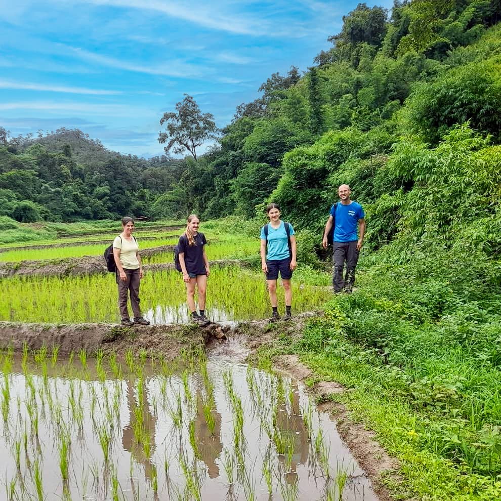 Trek group beside terraced rice paddies in a lush mountain valley.