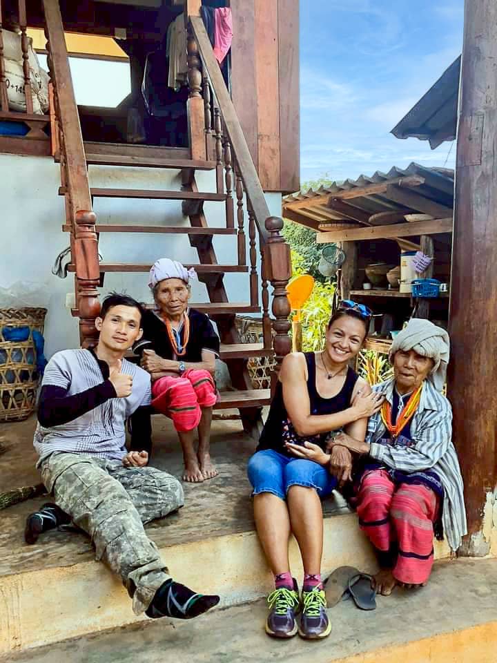 Guests with two local elders on a wooden porch in a mountain village during a Chiang Mai trekking visit.
