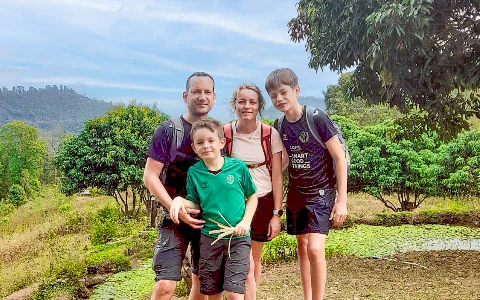 Family of four standing outdoors during a mountain trek, smiling with forested hills in the background.