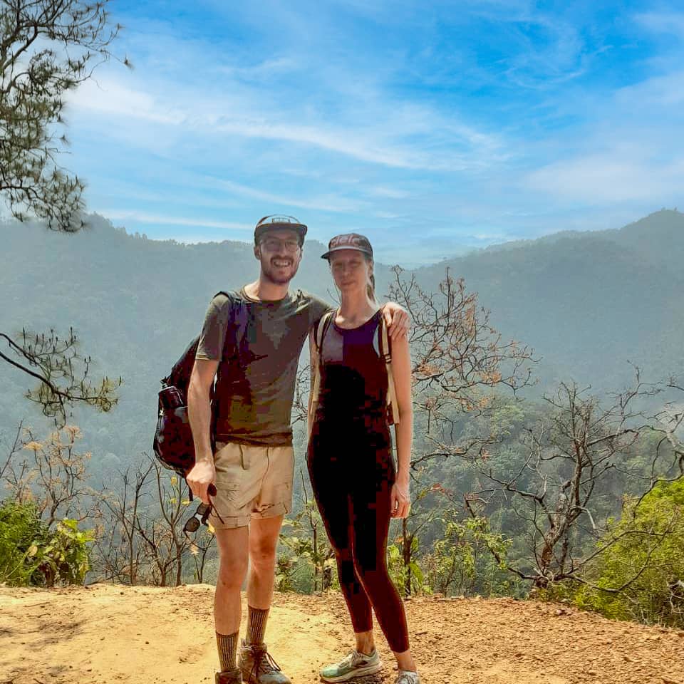 Young couple on a mountain trekking trail with backpacks and scenic misty valley behind